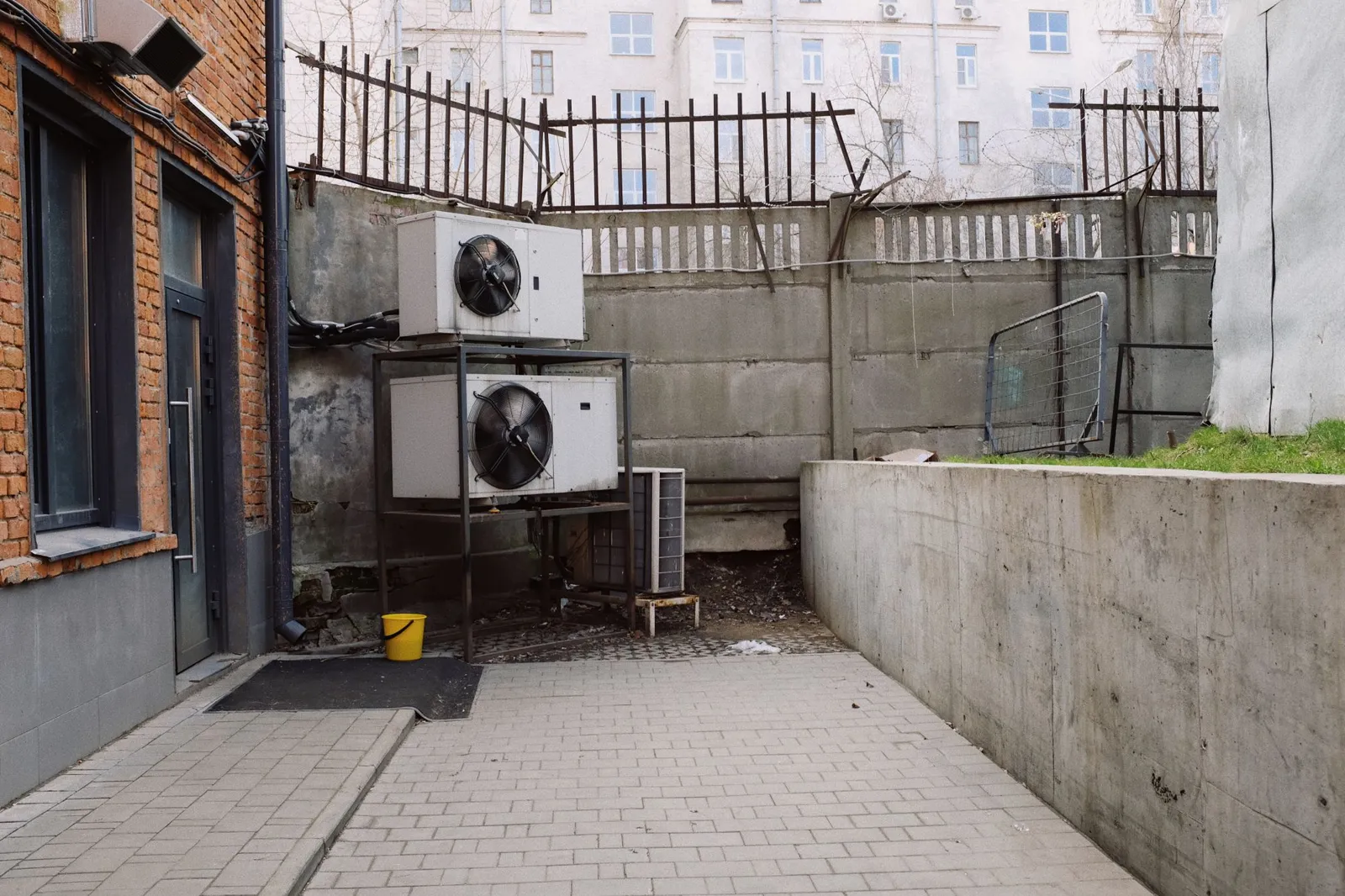 Two outdoor AC condenser units on a stand behind a building